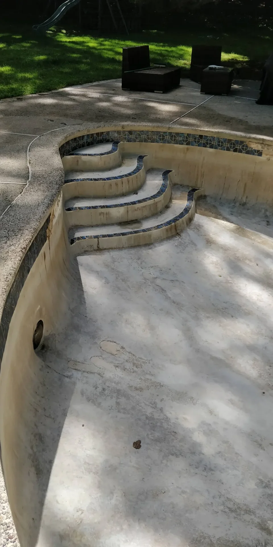Empty pool with worn plaster and tiled steps awaiting resurfacing
