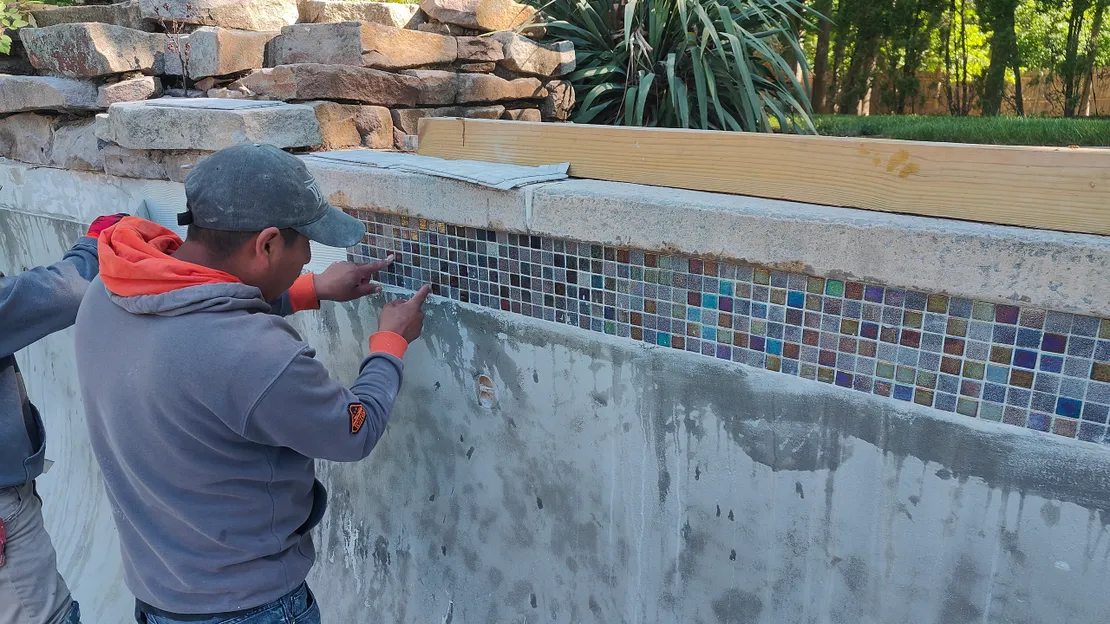 Worker installing iridescent glass mosaic tiles on a pool wall