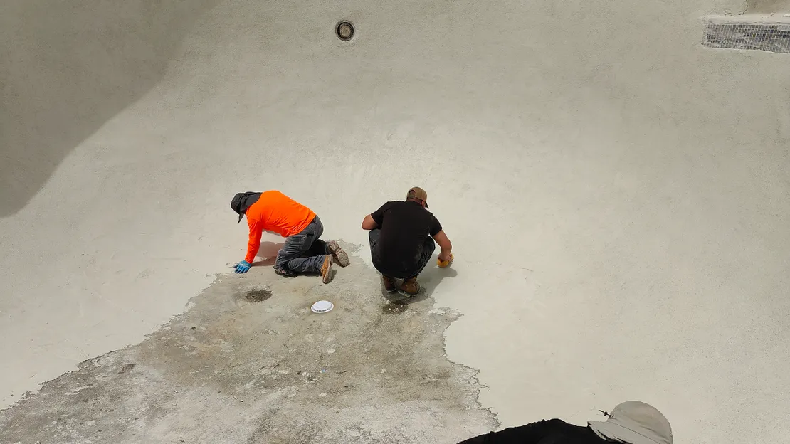 Two workers patching and prepping the floor of an empty pool