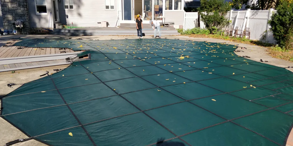 Green safety cover stretched over a backyard pool with fall leaves