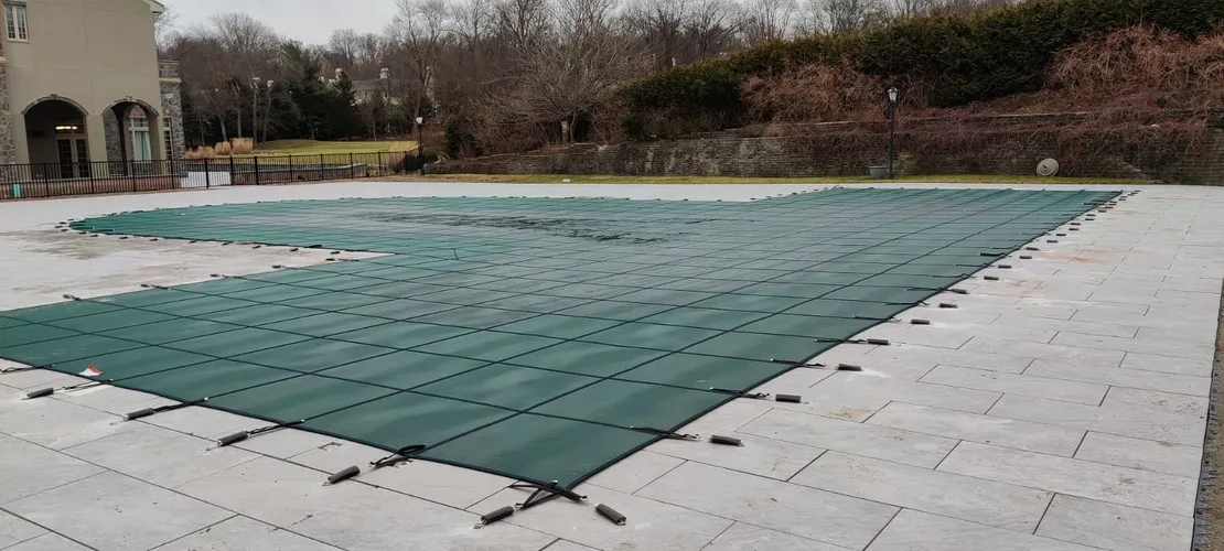 Green Kayden safety cover anchored across a large rectangular pool