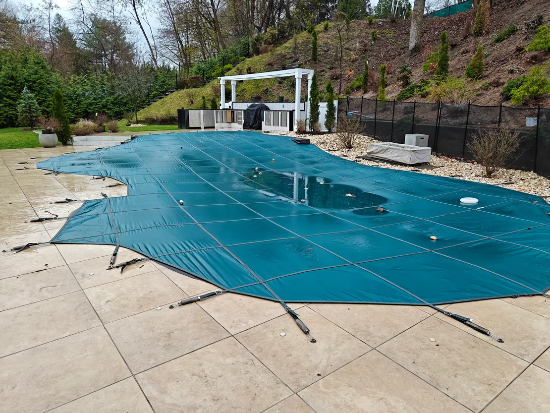 Teal safety cover on a custom-shape pool with stone patio