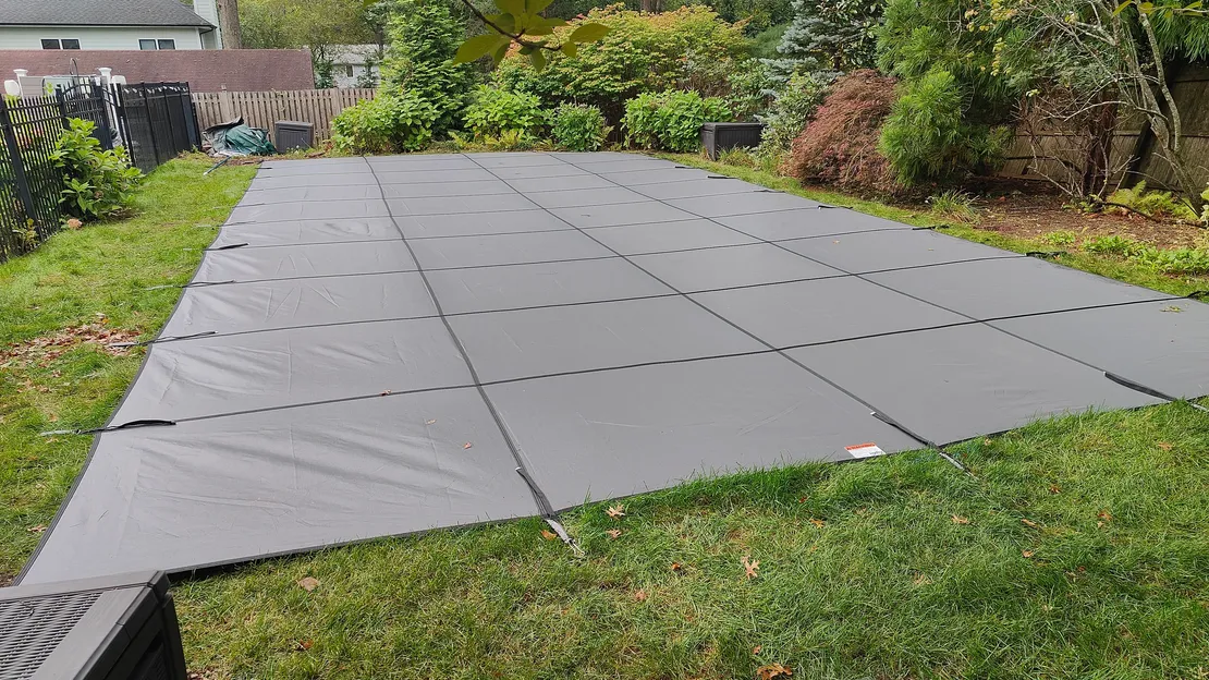 Gray safety cover stretched tightly over a rectangular backyard pool