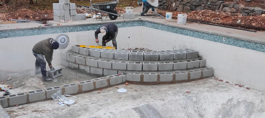 Workers building cinder block walk-in steps inside a pool