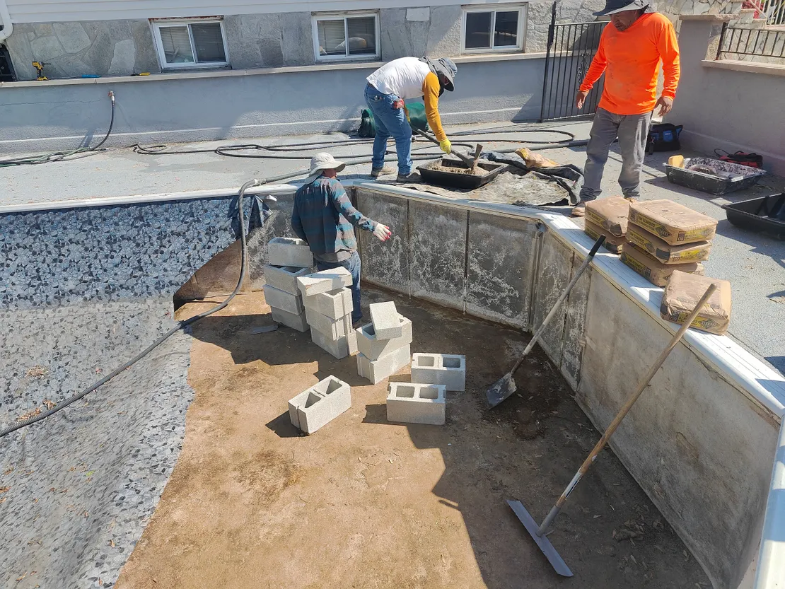 Crew building cinder block steps in a pool with fresh liner backing