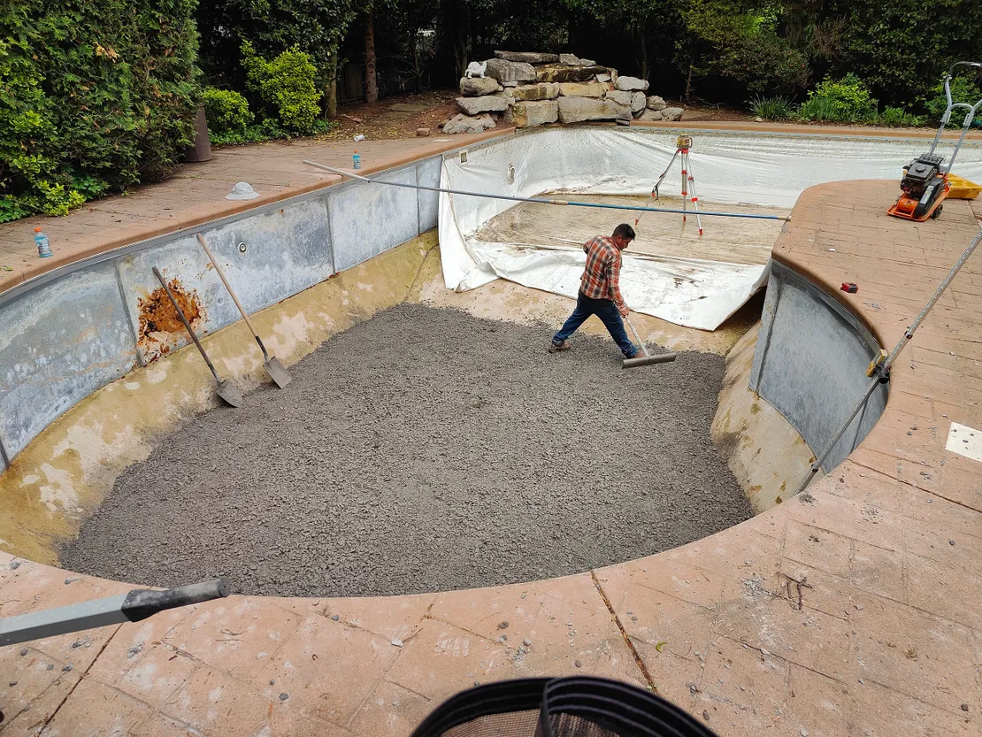 Worker spreading gravel base in an empty pool under renovation
